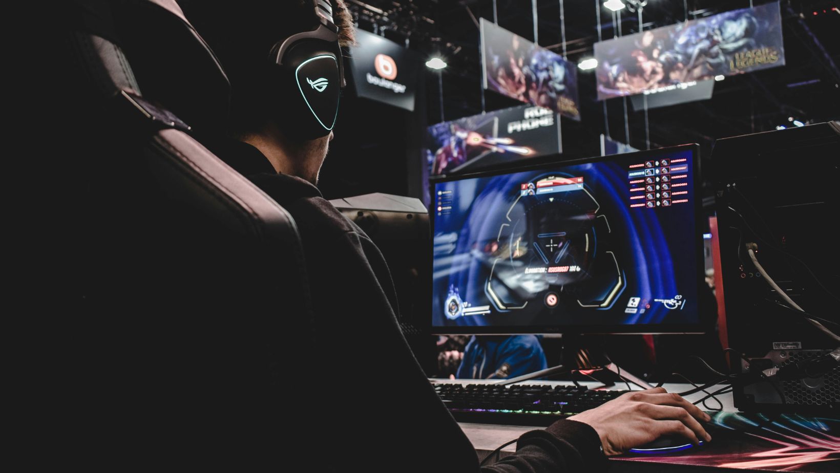 A gamer wearing headphones playing a game on a desktop computer at an event